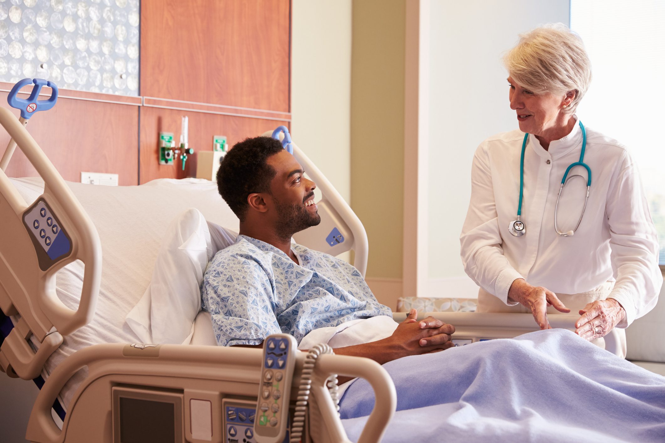 Female Doctor Talking To Male Patient In Hospital Bed